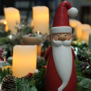 Adventsgestecke mit angezündeten Kerzen und einem Ton-Weihnachtsmann