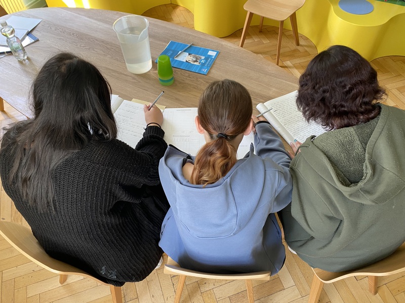 Drei Mädchen über einen Tisch gebeugt schreiben ihre Texte