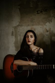 Sängerin Jaqueline Rubino mit Gitarre vor einer Betonwand
