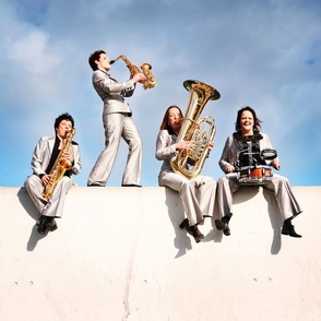 Band spielt "Open-Air" auf einer Betonmauer unter blauem Himmel