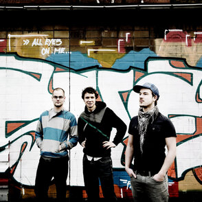 Gruppenfoto der drei Künstler vor einem Grafitti